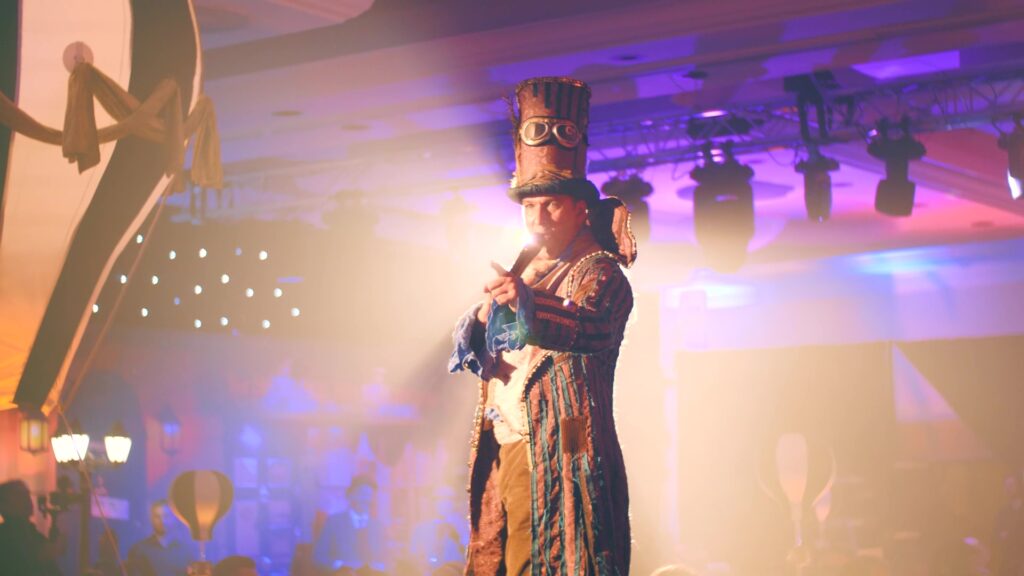 Een presentator in steampunk kleding en hoge hoed wijst de weg vanaf het podium